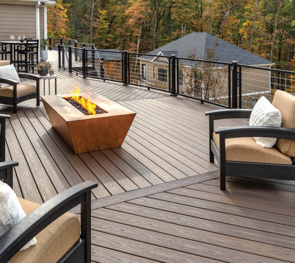 Spacious wooden deck with modern fire pit, surrounded by cushioned chairs. Autumn trees in the background create a cozy, inviting atmosphere.